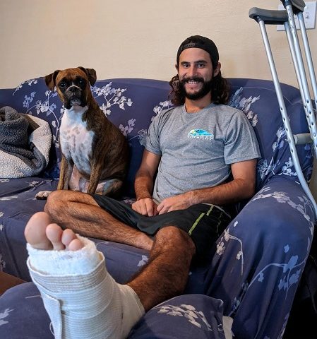 Stephen Michelena shows his shark bitten foot, while his dog Sophie watches over him. 